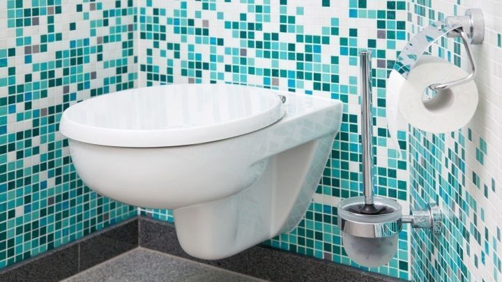 Ein WC-Deckel steht an einer Wand mit blauen Mosaikfliesen, umgeben von einem modernen Badezimmer-Design.