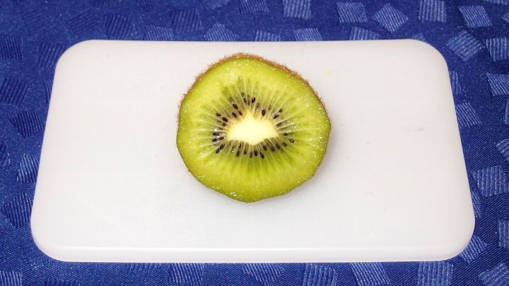 Eine geschnittene Kiwi liegt auf einem hellen Schneidebrett, bereit f&uuml;r die Verwendung als Fleischzartmacher in der K&uuml;che.