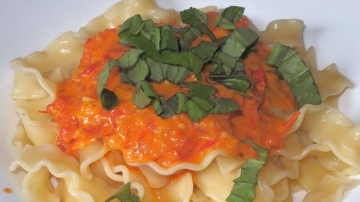 Eine Nudelgericht mit Creme Fraiche So&szlig;e ist auf einem wei&szlig;en Teller angerichtet, garniert mit frischem Basilikum.