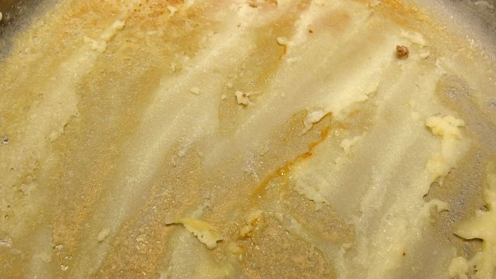 Ein angebrannter Topfboden zeigt eine gleichm&auml;&szlig;ige, goldbraune Schicht, die beim Kochen in der K&uuml;che entstanden ist.