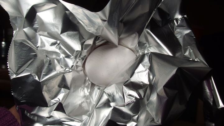 Ein zerknittertes St&uuml;ck Alufolie umschlie&szlig;t ein wei&szlig;es Ei, das in der Mitte liegt, und suggeriert eine kreative Kochmethode.