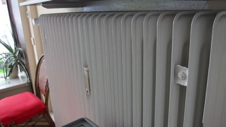 Ein Heizk&ouml;rper ist am Fenster montiert und gibt W&auml;rme ab, w&auml;hrend ein roter Stuhl im Hintergrund steht.