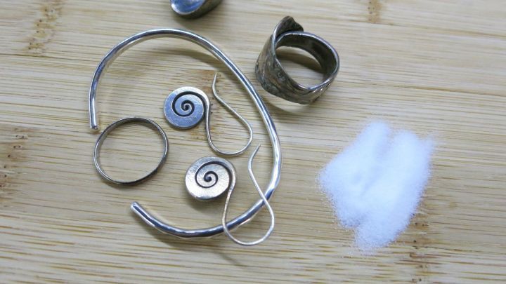 Silberringe und -anh&auml;nger liegen auf einem Holztisch, w&auml;hrend Calciumcarbonat in Form von Pulver daneben verstreut ist.