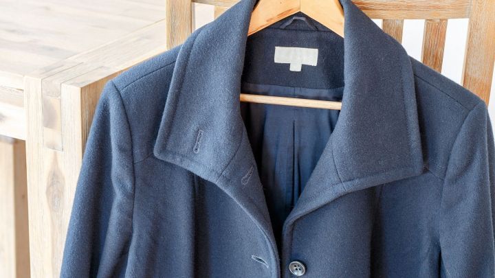 Ein hochwertiger Mantel h&auml;ngt an einem Holzstuhl in einem hellen Raum. Keine Textinformationen sichtbar.