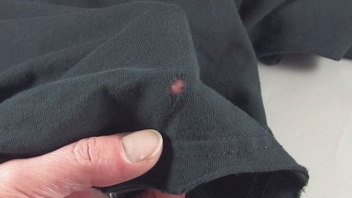 Ein Hand h&auml;lt ein schwarzes Kleidungsst&uuml;ck mit einem kleinen Loch, was auf Mottensch&auml;den hinweist. Ein Hinweis auf &bdquo;Motten&ldquo;.