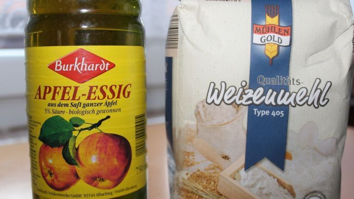 Eine Flasche Apfelessig steht neben einem Sack Weizenmehl, bereit zur Anwendung gegen Dornenwarzen in der K&uuml;che.