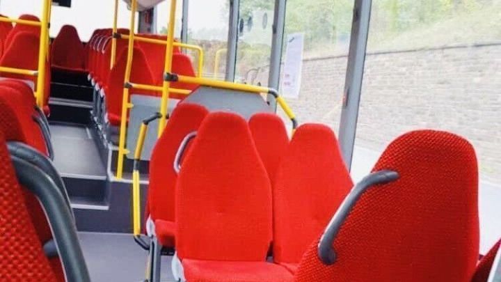 Rote Sitze in einem leeren Bus, der stillsteht und durch gro&szlig;e Fenster eine gr&uuml;ne Umgebung zeigt, ideal f&uuml;r g&uuml;nstiges Reisen.