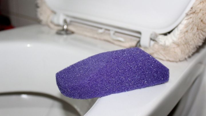 Ein lila Reinigungsschwamm liegt auf dem Rand einer Toilette und wartet darauf, Kalk und Urinstein zu entfernen.