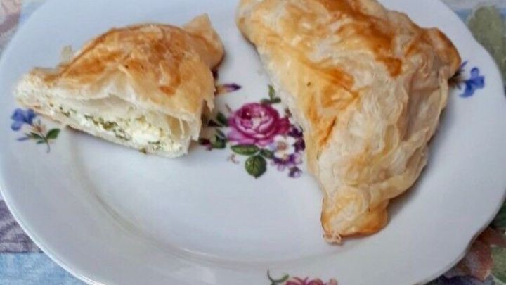 Zarte gef&uuml;llte Bl&auml;tterteigtaschen liegen auf einem blumengeschm&uuml;ckten Teller, w&auml;hrend eine H&auml;lfte leicht angeschnitten ist.