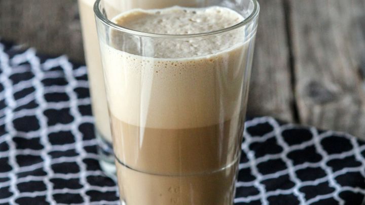 Ein gro&szlig;es Glas Iced Caro steht auf einem karierten Tuch. Es hat eine schaumige Schicht oben und eine cremige braune Farbe.