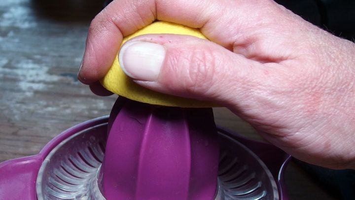 Eine Hand presst eine Zitrone in einen lila Entsafter, um frischen Zitronensaft zu gewinnen.