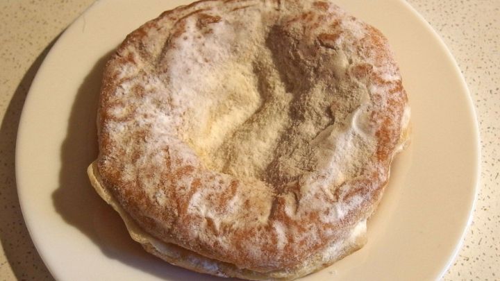 Ein goldbrauner Bauernkrapfen liegt auf einem wei&szlig;en Teller, umgeben von einer einfachen K&uuml;chenoberfl&auml;che.