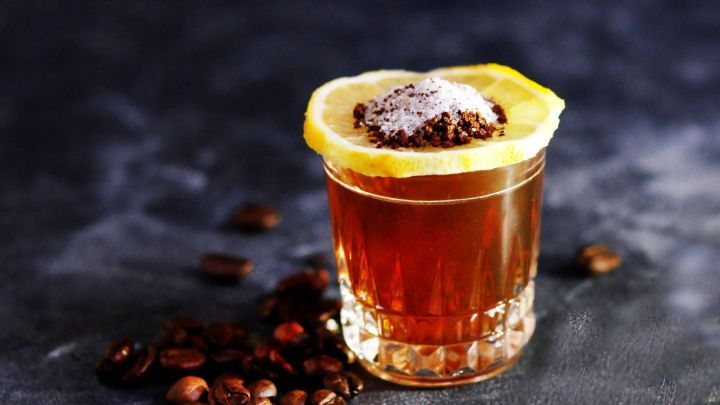 Ein Glas mit einem Getr&auml;nk aus Koffein und Alkohol, garniert mit einer Zitronenscheibe, steht auf einem dunklen Hintergrund.