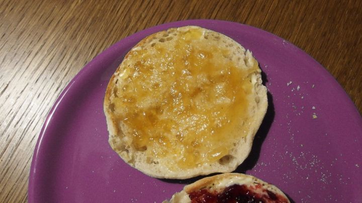Eine goldene Marmelade liegt auf einem Br&ouml;tchen, das auf einem lila Teller in einer gem&uuml;tlichen Umgebung serviert wird.