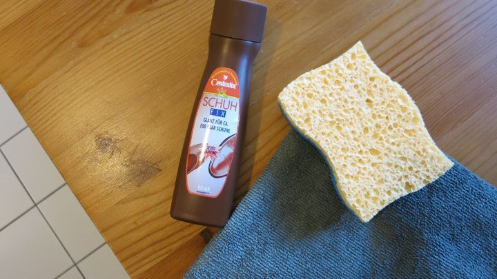 Ein Fl&auml;schchen Schuhcreme steht neben einem Schwamm auf einem Holztisch, bereit zum Polieren dunkler M&ouml;bel.