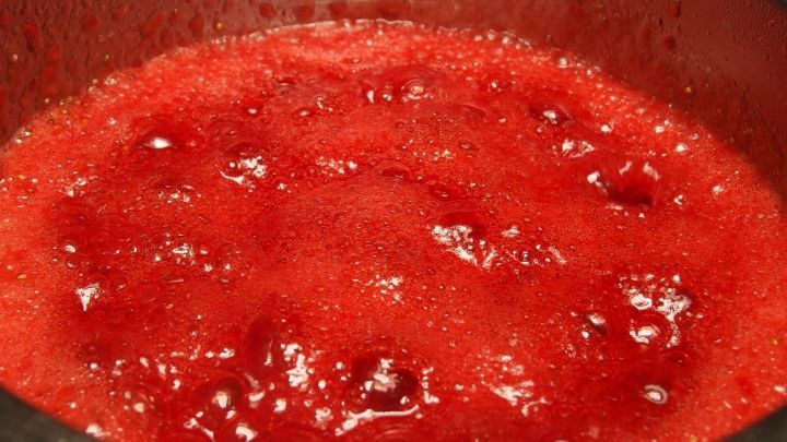 Leuchtend rote Erdbeermarmelade kocht sprudelnd in einem Topf, umgeben von einer gem&uuml;tlichen K&uuml;chenatmosph&auml;re.