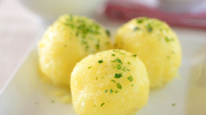 Drei gelbe Kl&ouml;&szlig;e mit Kr&auml;utern liegen auf einem wei&szlig;en Teller, umgeben von Schalen mit weiteren Beilagen.