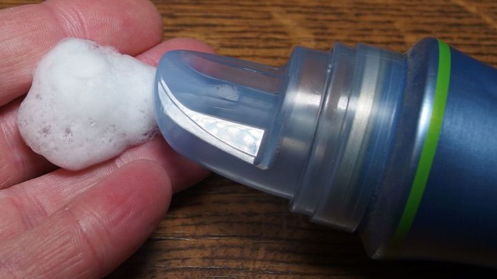 Eine Hand h&auml;lt eine Portion Schaumfestiger, um Kaugummi aus den Haaren zu entfernen, auf einem Holztisch.