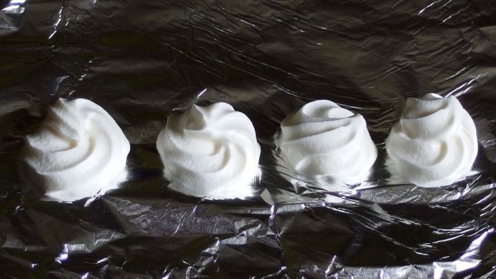 Kleine Tuffs aus Schlagsahne liegen auf Aluminiumfolie und warten darauf, eingefroren zu werden.