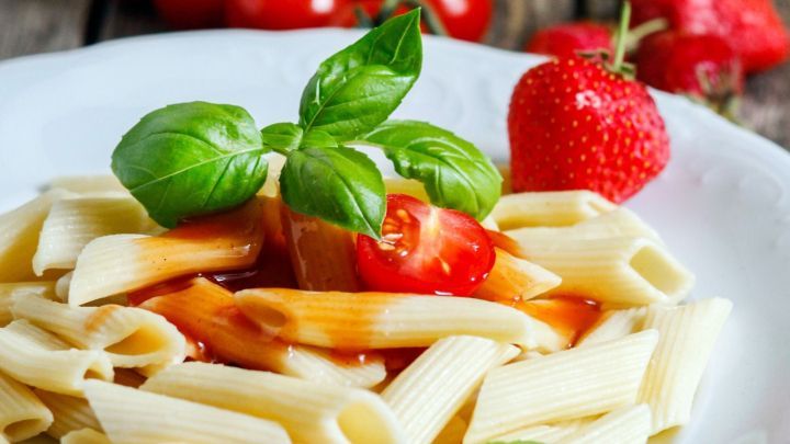 Ein Teller mit Pasta ist mit einer Erdbeer-Tomaten-Sauce und frischem Basilikum garniert, umgeben von reifen Tomaten und Erdbeeren.