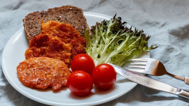 Auf einem Teller liegen Zucchinipuffer ohne Ei, begleitet von frischem Salat, Tomaten und Vollkornbrot.