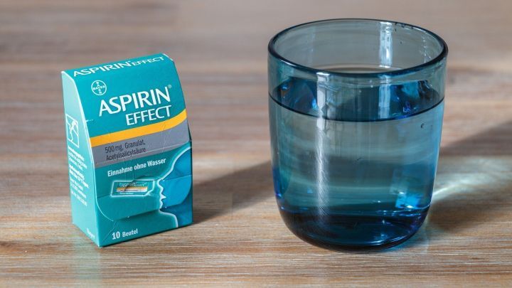 Ein blauer Becher mit Wasser steht neben einer kleinen Packung Aspirin. Es scheint so, als ob er f&uuml;r die Einnahme bereit ist.