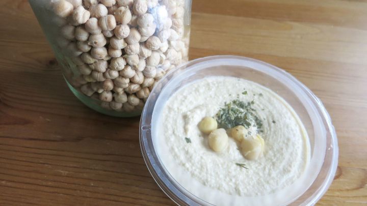Kichererbsenmus liegt in einer Schale, w&auml;hrend ein Glas mit ungesch&auml;lte Kichererbsen daneben steht.