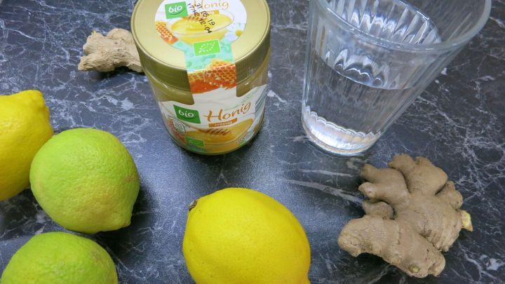 Frische Ingwerwurzel, Zitronen und ein Glas Wasser liegen auf einer dunklen Oberfl&auml;che zur Zubereitung eines Vitamindrinks.