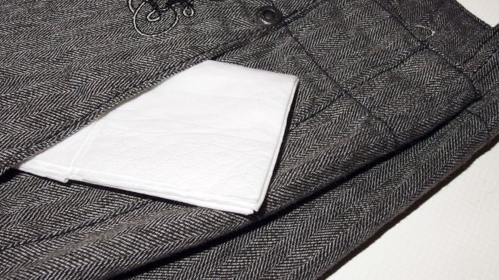 Ein Papiertaschentuch liegt auf grauen Stoffhosen, bereit, Fusseln zu entfernen, möglicherweise nach dem Trocknen.