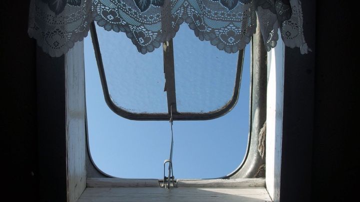 Ein Dachfenster im ge&ouml;ffneten Zustand zeigt den blauen Himmel, umgeben von einer Spitzenvorhang. Es wirkt schmutzig und ben&ouml;tigt Reinigung.