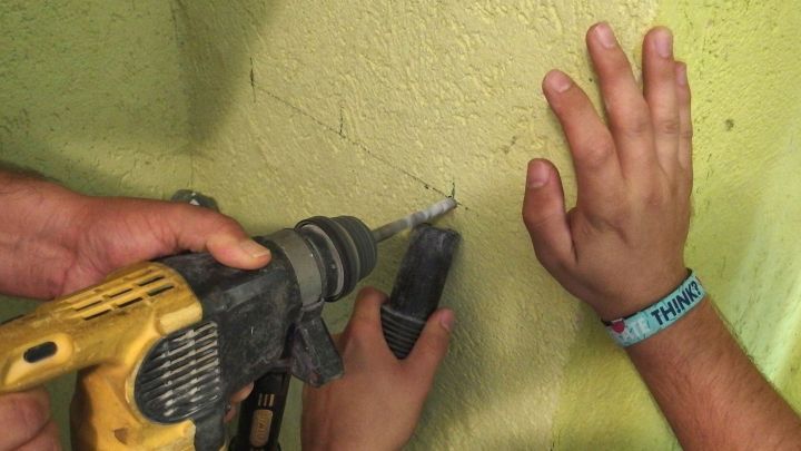 Ein Bohrer wird sicher an einer Wand positioniert, w&auml;hrend eine Hand das Werkzeug h&auml;lt und eine andere Hand bereit ist.