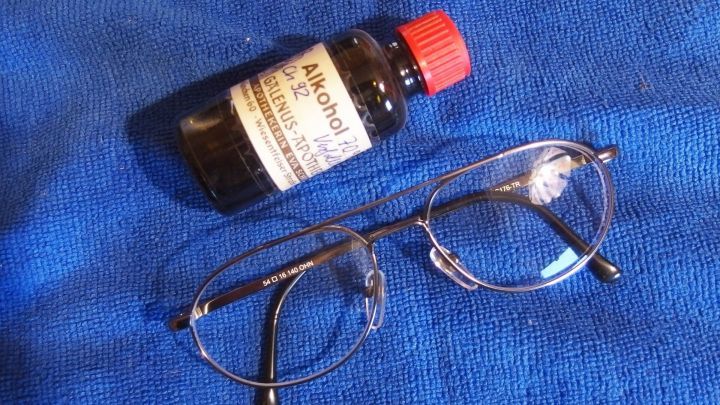 Eine Brille liegt auf einem blauen Tuch, neben ihr steht eine Flasche Alkohol, bereit zum Putzen der Gl&auml;ser.