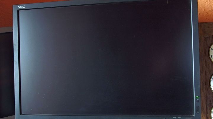 Ein glatter, schwarzer Bildschirm zeigt kein Bild und steht auf einem Tisch in einem warmtonigen Raum.