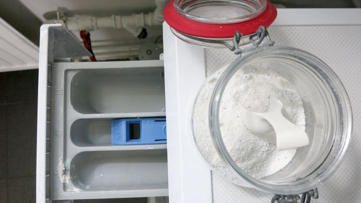 Ein Waschmaschinenfach mit einem lila Einleger und einem offenen Glas mit Waschpulver daneben, bereit zum Bef&uuml;llen.