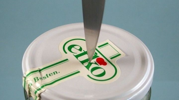 Ein Messer ist auf den Deckel eines Glases gerichtet, um ihn ganz leicht zu &ouml;ffnen. Der Hintergrund ist neutral.