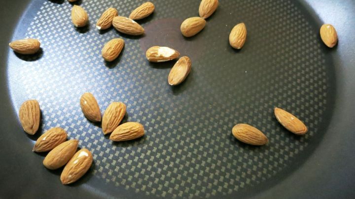 Mandeln liegen verstreut in einer Bratpfanne, bereit zum R&ouml;sten, um den Geschmack f&uuml;r Nusskuchen zu intensivieren.