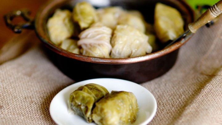 Kohlrouladen auf einem Teller neben einem Kupfertopf serviert; sie liegen auf einem rustikalen Leinentuch im Hintergrund.