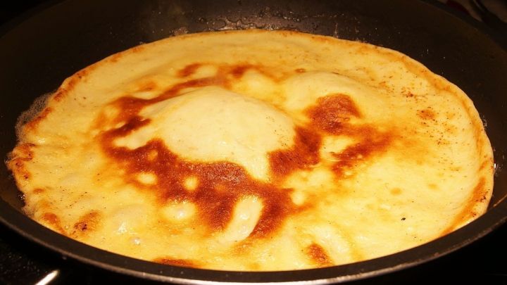 Ein Pfannkuchen br&auml;t in einer Pfanne, w&auml;hrend er goldbraun und knusprig wird, ganz ohne Eier.