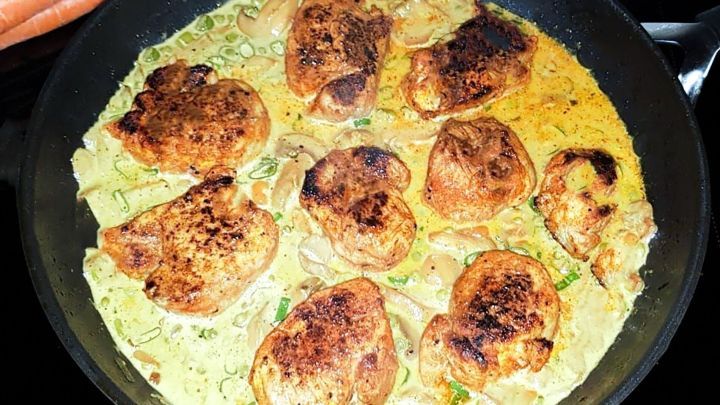 Schweinemedaillons braten in einer Curry-Banane-So&szlig;e in einer Pfanne, umgeben von frischen Karotten.