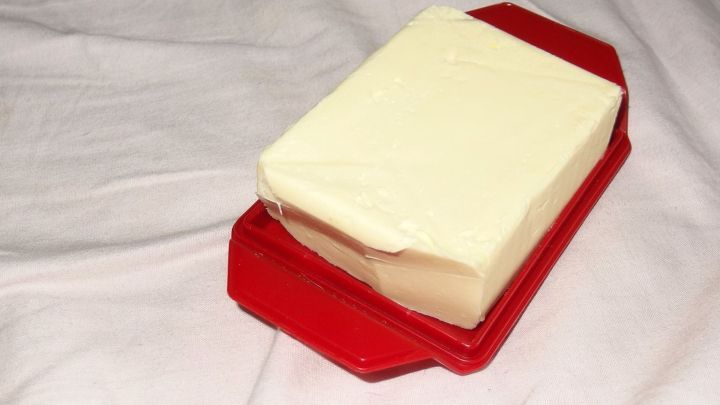 Ein St&uuml;ck Butter liegt auf einem roten Buttergeschirr, umgeben von einem wei&szlig;en Tuch, bereit zum Auftragen.