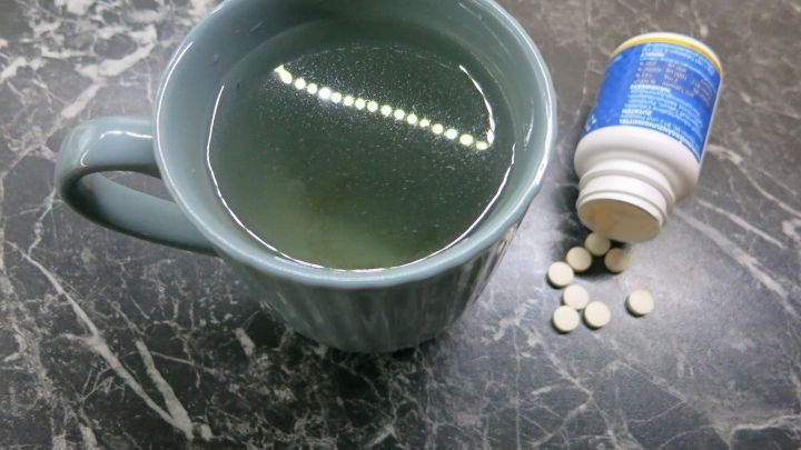 Eine Tasse mit gr&uuml;nem Tee steht auf einem Tisch, neben einem umgekippten Fl&auml;schchen Vitamintabletten.