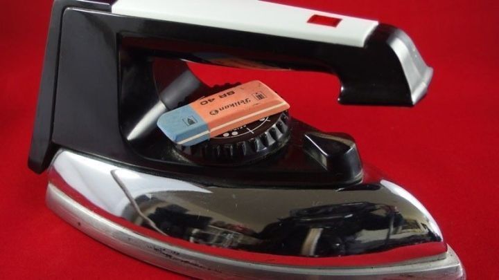 Ein B&uuml;geleisen steht auf einer roten Oberfl&auml;che, w&auml;hrend ein Radiergummi darauf liegt, um es zu reinigen.