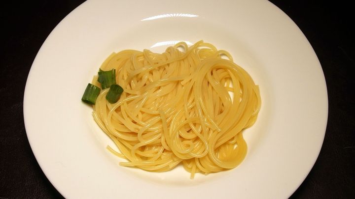 Ein Teller mit Spaghetti liegt auf einem Tisch, die Nudeln sind locker angerichtet und mit gr&uuml;nen Kr&auml;utern garniert.