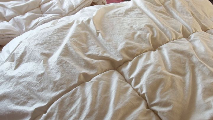 Wei&szlig;es Daunenbett liegt unordentlich auf einem Bett, bereit zum Waschen mit Essig-Essenz f&uuml;r frische Pflege.