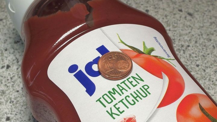 Ein Cent-St&uuml;ck liegt auf einer Ketchup-Flasche, um die M&uuml;nzen mit Ketchup zu polieren, auf einer grauen Oberfl&auml;che.