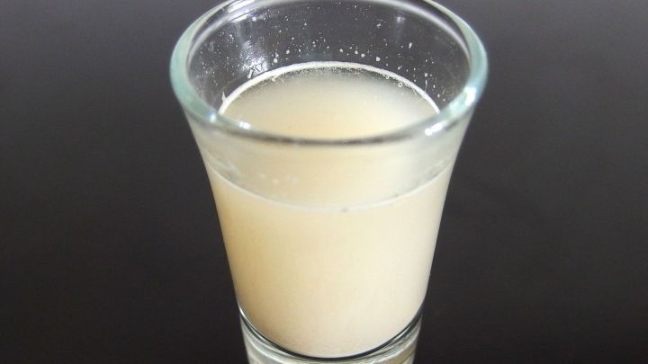 Ein klarer Shot-Glas mit einer tr&uuml;ben Fl&uuml;ssigkeit darin steht auf einer dunklen Oberfl&auml;che, w&auml;hrend M&uuml;ckenstiche mit Bierhefe verhindert werden sollen.