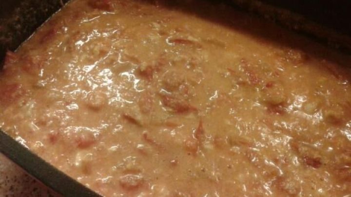 Tomaten schmoren in einer schwarzen Pfanne, umgeben von einer dicken, roten Sauce auf einer K&uuml;chenarbeitsplatte.