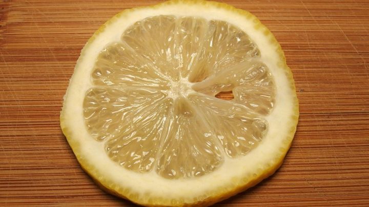 Eine Zitronenscheibe liegt auf einem Holzbrett und eignet sich zur Anwendung gegen eine verbrannte Zunge.