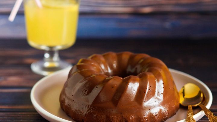 Eine gl&auml;nzende, schokoladige Bombe auf einem wei&szlig;en Teller wird von einem erfrischenden, gelben Getr&auml;nk im Hintergrund begleitet.