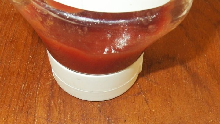 Eine Ketchupflasche steht auf einem Holztisch, der Ketchup flie&szlig;t heraus und hinterl&auml;sst einen unordentlichen Rand.